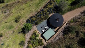 An aerial view of a house with a circular roof structure, a green-roofed building, and a small pond. - Awaawa Yurts - Papa - Our Island (Waiheke Island)