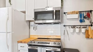 Una cocina moderna con armarios blancos, un microondas de acero inoxidable, una estufa a gas y un cubo de basura.