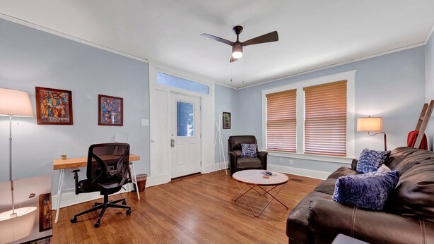 A spacious living room with hardwood flooring, a ceiling fan, a brown leather couch, a round coffee table, and a desk with a chair. - Evergreen Historic District 1928 Midtown Apartment (Memphis)