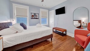 A bedroom with a bed, a bench, a chair, a ceiling fan, and a TV mounted on the wall. - Evergreen Historic District 1928 Midtown Apartment (Memphis)