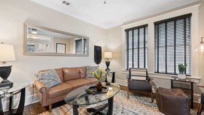 Un salon avec un canapé en cuir marron, une table basse en verre, un tapis à motifs, une table d’appoint avec une lampe et un fauteuil.