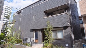 A modern apartment building with a grey facade, multiple balconies, and a small garden area with plants and a bicycle. - GRANDBASESUMIYOSHI (Fukuoka)