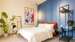 A modern bedroom with a bed, a mirror, a colorful abstract painting, a plant, and a metal shelf unit. - Floris - Sophisticated Studio (Bari)