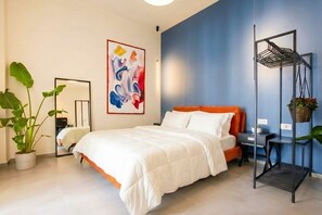 A modern bedroom with a bed, a mirror, a colorful abstract painting, a plant, and a metal shelf unit. - Floris - Sophisticated Studio (Bari)