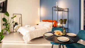 A modern hotel room with a bed, a dining table with plates and bread, a hanging plant, and a TV. - Floris - Sophisticated Studio (Bari)