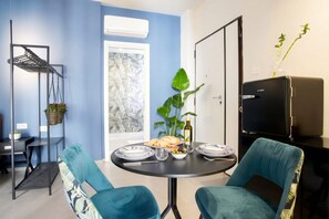 A dining area with a round table, two chairs, a black grill, a plant, and a window with a view. - Floris - Sophisticated Studio (Bari)