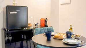 A compact kitchen with a coffee machine, a small refrigerator, a dining table with a blue chair, and a vase with green plants. - Floris - Sophisticated Studio (Bari)
