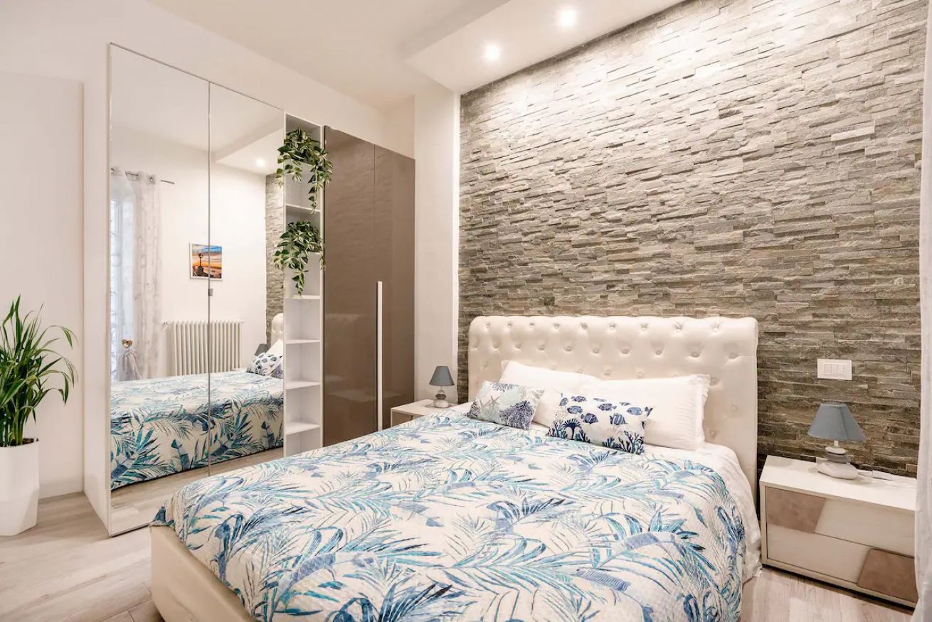 A bedroom with a mirrored wardrobe, a stone accent wall, and a bed with a floral bedspread.