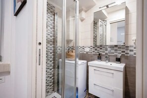 Um banheiro moderno com box de vidro, pia branca com espelho e painel de azulejos.