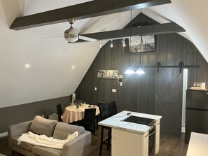 A cozy loft-style room with a dining area, kitchenette, and a ceiling fan.