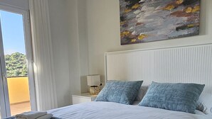 Une chambre avec un grand lit, une vue sur l’extérieur, un tableau au mur et un luminaire au plafond.