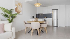 A modern kitchen with white cabinets, a stainless steel refrigerator, and a dining area with a round table and four chairs. - Casa de los amigos Sea View Estepona (Málaga)