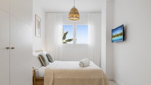 A bedroom with a bed, a window with curtains, a television, and a framed picture on the wall. - Casa de los amigos Sea View Estepona (Málaga)