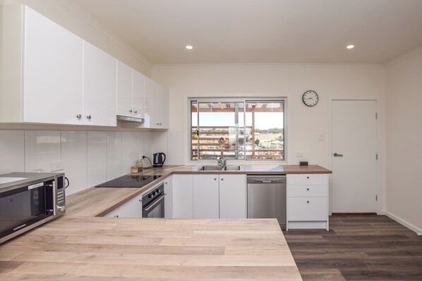 A modern kitchen with white cabinets, a wooden countertop, a stainless steel dishwasher, and a window with a view of a parking lot. - Sunset Hideaway - In Kingscote (Kingscote)