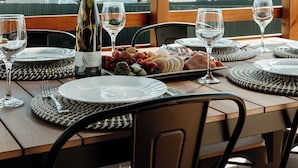 A dining table set with plates, glasses, and a bottle of wine, with a view of trees and buildings in the background. - Sunset Hideaway - In Kingscote (Kingscote)