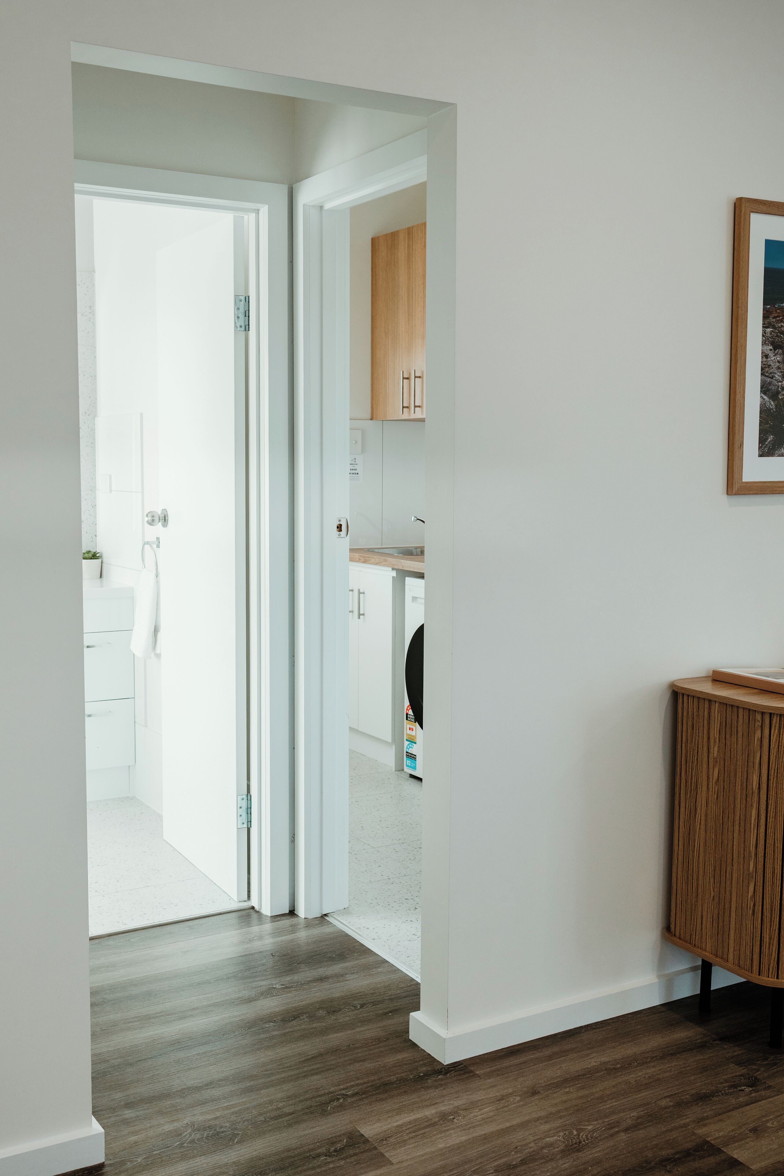 A hallway with a wooden floor, white walls, and a wooden cabinet.