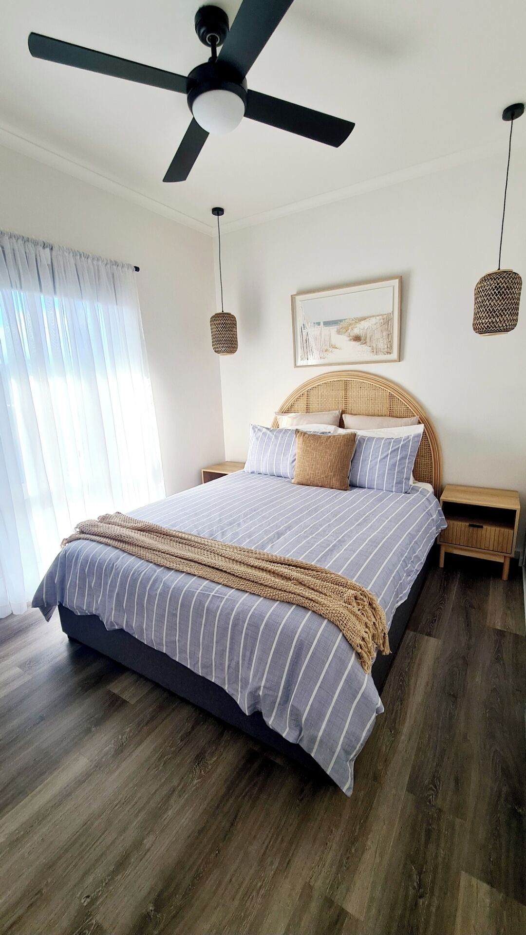 A bedroom with a bed, a ceiling fan, a bedside table, a nightstand, and a window with curtains.