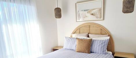 A bedroom with a bed, a ceiling fan, a bedside table, a nightstand, and a window with curtains.