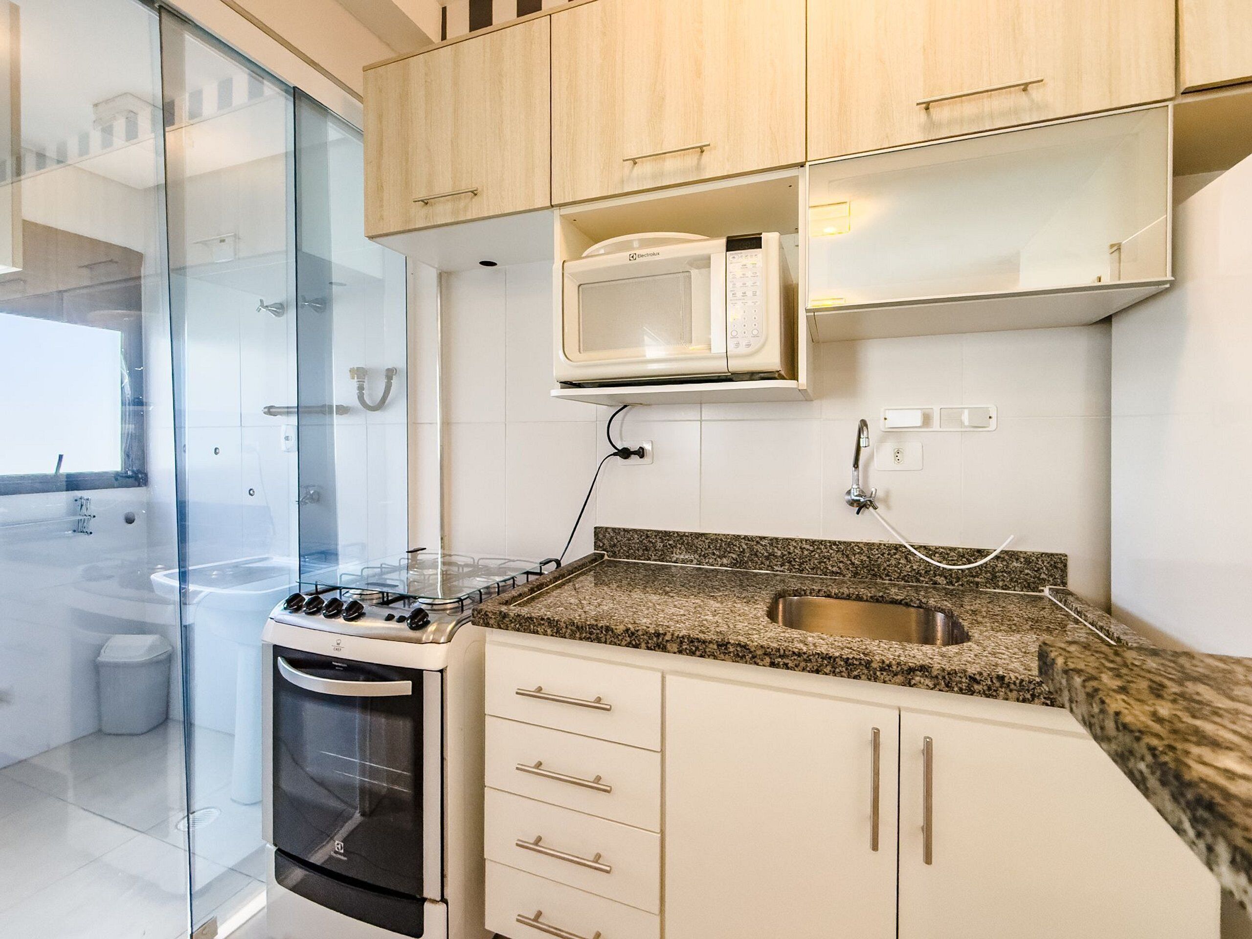 A modern kitchen with a built-in oven, microwave, granite countertop, stainless steel sink, and white cabinetry.