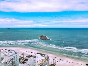 Un hotel costero con varios pisos, vista a la playa y un promontorio rocoso en el mar.