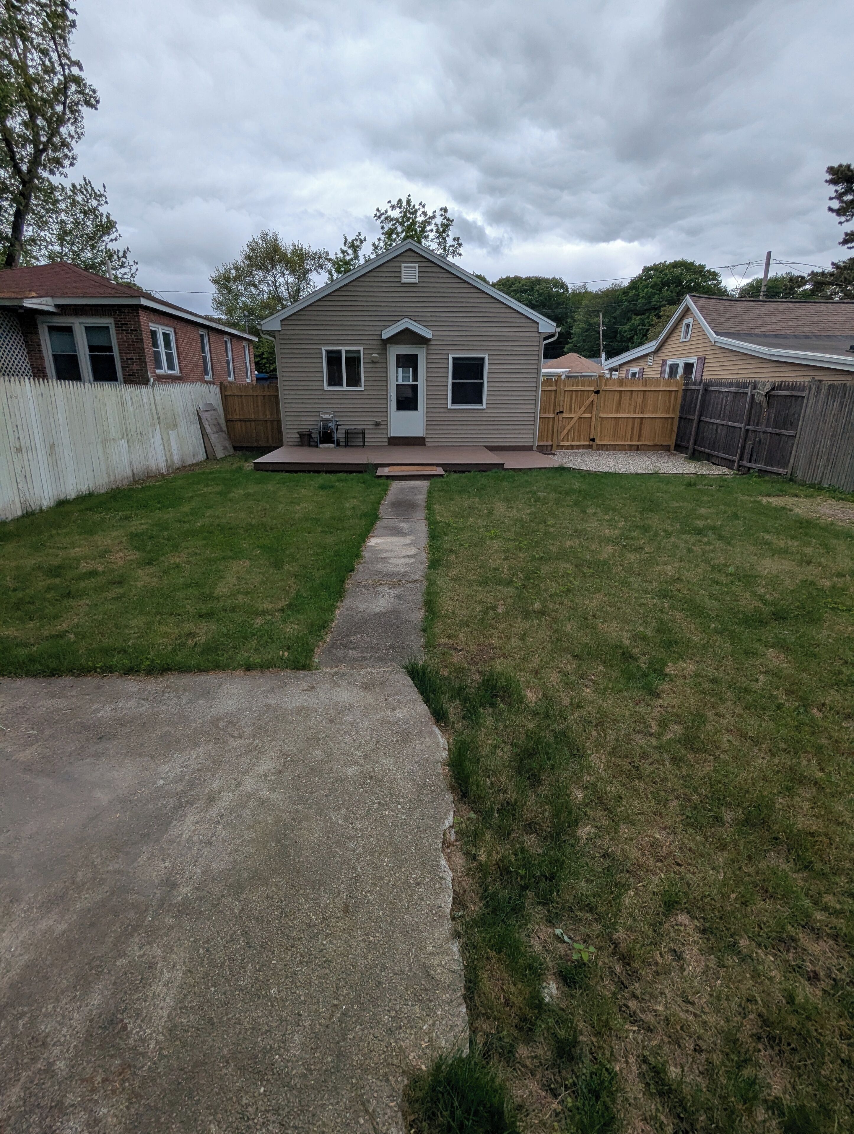 A residential backyard with a house, a wooden fence, and a concrete pathway.