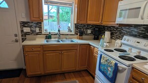 A kitchen with wooden cabinets, a white stove, a microwave, and a window with a view of the outdoors. - Cottage in Warwick (Warwick)