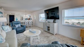 A modern living room with a flat-screen TV, a dining area, and a view of the ocean.