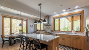 A modern kitchen with a large island, wooden cabinets, and large windows offering a view of the outdoors. - Lakeways A-Frame Near Lake James Game Room · Gym · Golf · Fire Pit · Sleeps 10 (Nebo)