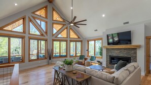 A spacious living room with high ceilings, large windows, a fireplace, and a television. - Lakeways A-Frame Near Lake James Game Room · Gym · Golf · Fire Pit · Sleeps 10 (Nebo)