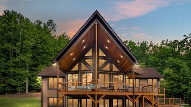 A modern cabin with a large deck and multiple windows, surrounded by a forest. - Lakeways A-Frame Near Lake James Game Room · Gym · Golf · Fire Pit · Sleeps 10 (Nebo)