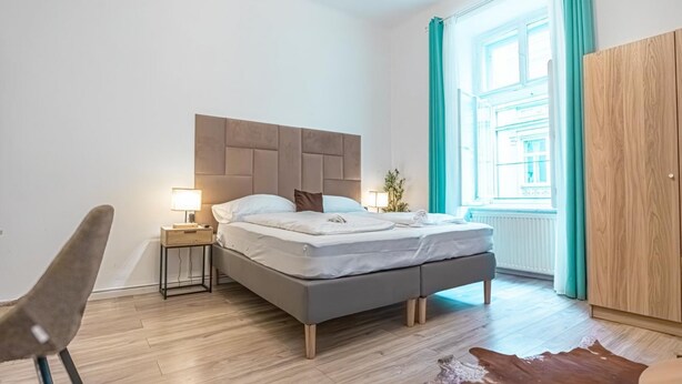 Un dormitorio moderno con cama, mesita de noche, lámpara y vistas al exterior.