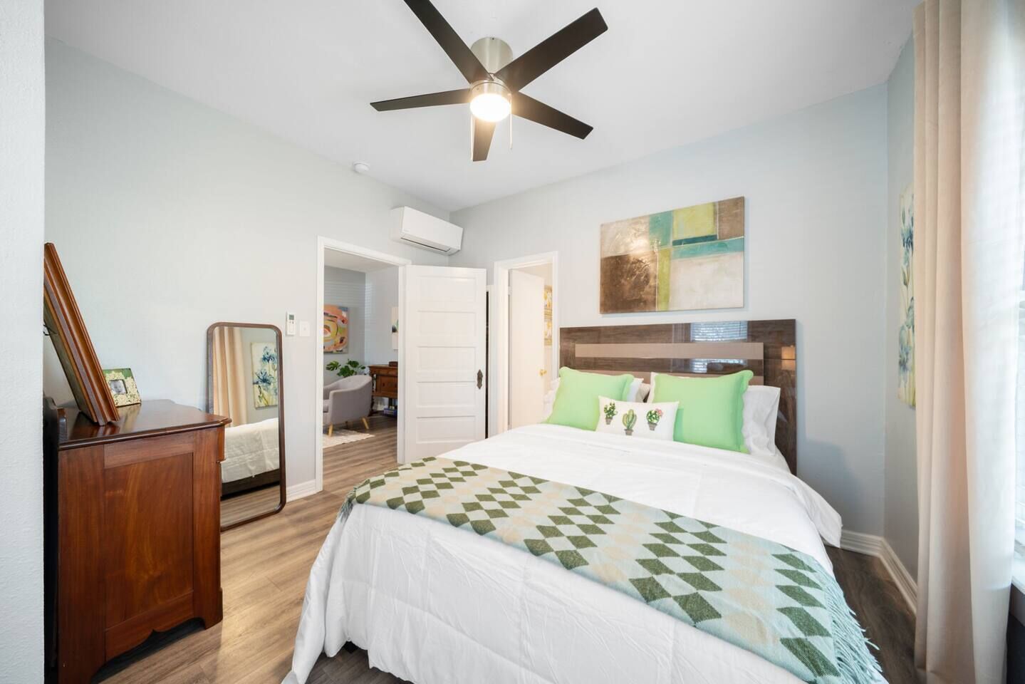 Ein Schlafzimmer mit Bett, Deckenventilator, Kommode und einer Tür zu einem anderen Raum.