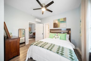 Une chambre à coucher comprenant un lit, un ventilateur de plafond, une commode et une porte donnant sur une autre pièce.