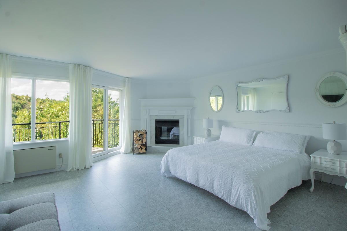 A spacious bedroom with a large bed, a fireplace, and a balcony with a view of greenery.
