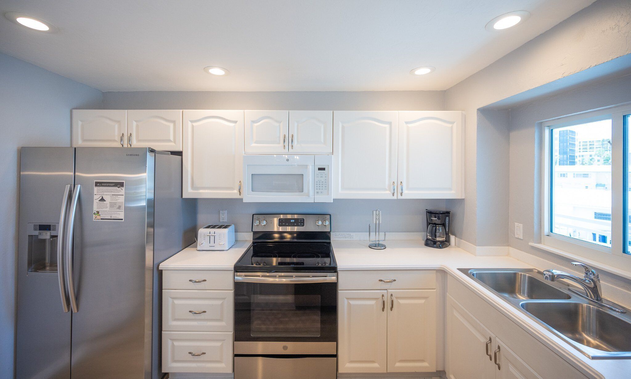 A modern kitchen with white cabinets, stainless steel appliances, a built-in microwave, a stove, and a sink.