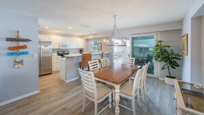Una cocina moderna con muebles blancos, una isla central y un comedor con mesa de madera y sillas blancas.