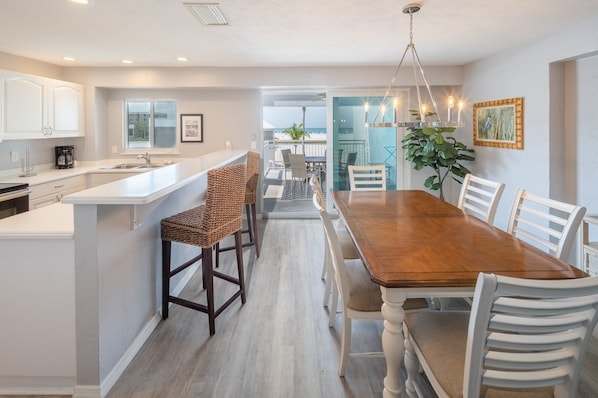 A modern kitchen with white cabinets, a wooden dining table, and a view to the outside. - Siesta Key Beachfront - 2BR Condo w/ Pools & Views (Siesta Key)