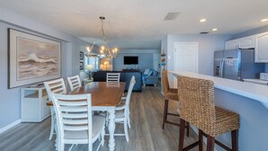 A modern kitchen with white cabinets, a stainless steel refrigerator, and a dining area with a wooden table and white chairs. - Siesta Key Beachfront - 2BR Condo w/ Pools & Views (Siesta Key)