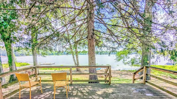 Terraza de madera con dos sillas de mimbre y un banco, con vista a un lago.