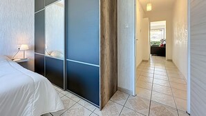 Un dormitorio con cama, mesita de noche, puerta corredera y vista hacia una sala de estar.