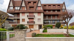 A modern multi-story residential building with a symmetrical facade, multiple balconies, and a well-maintained garden area.