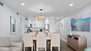 Una cocina moderna con armarios blancos, una zona de comedor con sillas estampadas y una consola de madera.