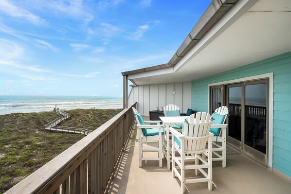 Ein Balkon mit Blick auf den Strand, weißen Adirondack-Stühlen und einem Tisch.