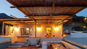A covered outdoor seating area with a pool, white furniture, and warm lighting.
