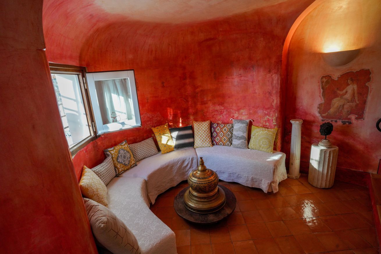 A cozy, curved sofa set against a vibrant red wall with a decorative metal object in the center.