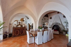 A spacious dining area with a wooden table and white chairs, surrounded by arches and a stone fireplace.