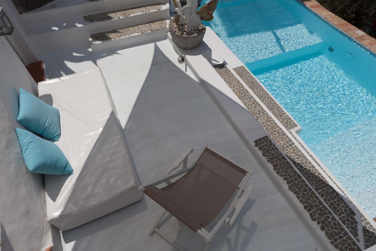 A poolside area with white lounge chairs, a small table, and a decorative stone planter.