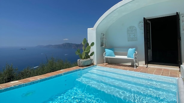 A poolside area with a view of the sea, a white bench with a cushion, and a cactus plant.