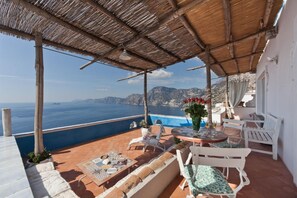 A terrace with a view of the sea, white furniture, and a table with a vase of flowers. - Amalfi Coast Enchanting Villa with terrace, pool and unique view (Praiano)