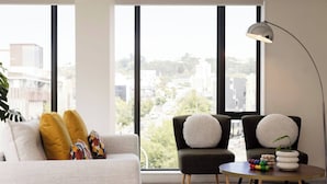 Een moderne woonkamer met een bank, twee fauteuils, een ronde salontafel en een vloerlamp. Grote ramen bieden uitzicht over de stad.